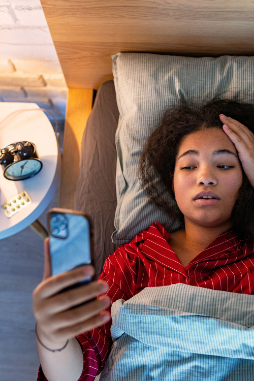 Woman in red pajamas lying in bed using a smartphone
